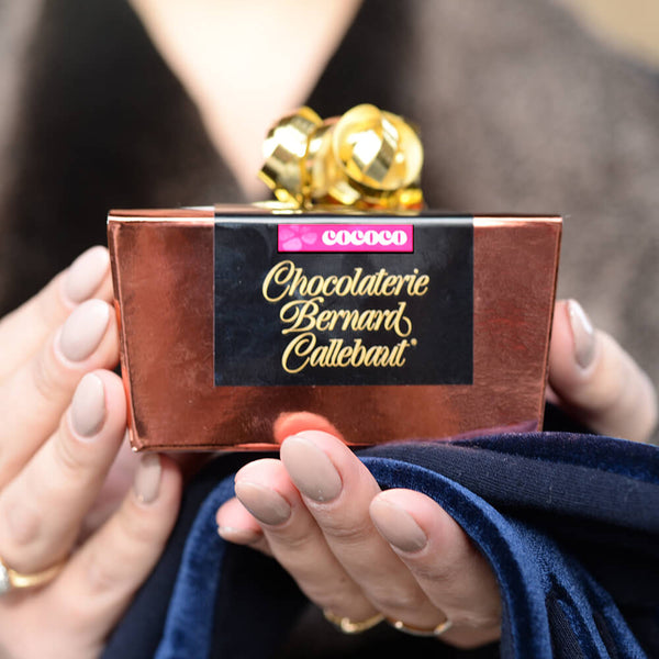 Hands holding Chocolaterie Bernard Callebaut® copper chocolate box with gold ribbon