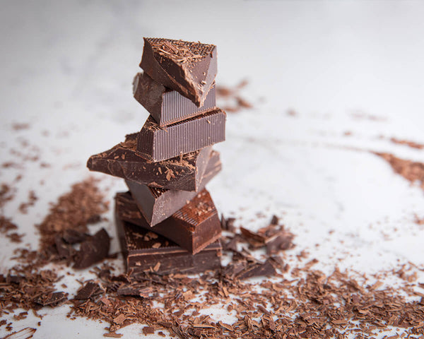 Chunks of vegan chocolate stacked on top of one another surrounded by chocolate shavings