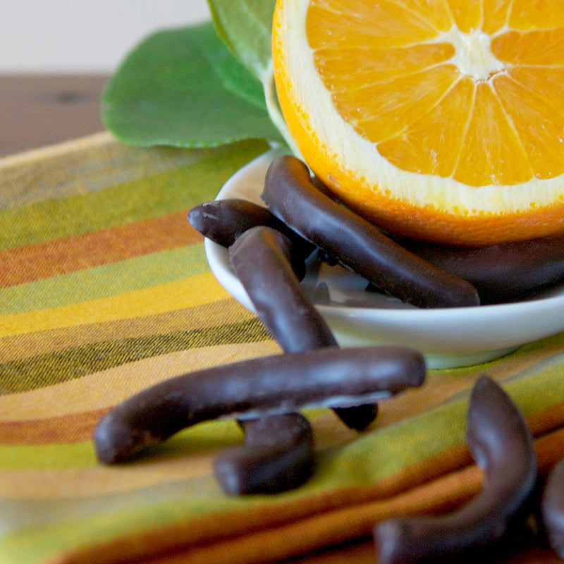 Dark chocolate coated orange peel with 1/2 orange on a green striped tablecloth