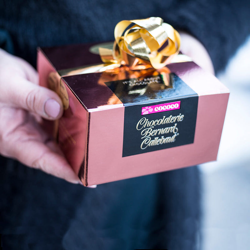 Hands holding a Chocolaterie Bernard Callebaut® copper box with gold ribbon