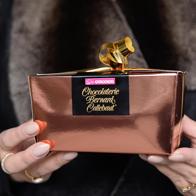 Hands holding a Chocolaterie Bernard Callebaut® copper chocolate box with gold ribbon