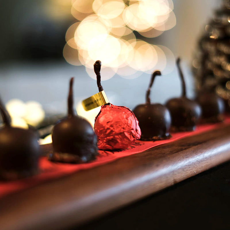 Tray of dark chocolate enrobed cherries with one cherry in the middle wrapped in red foil